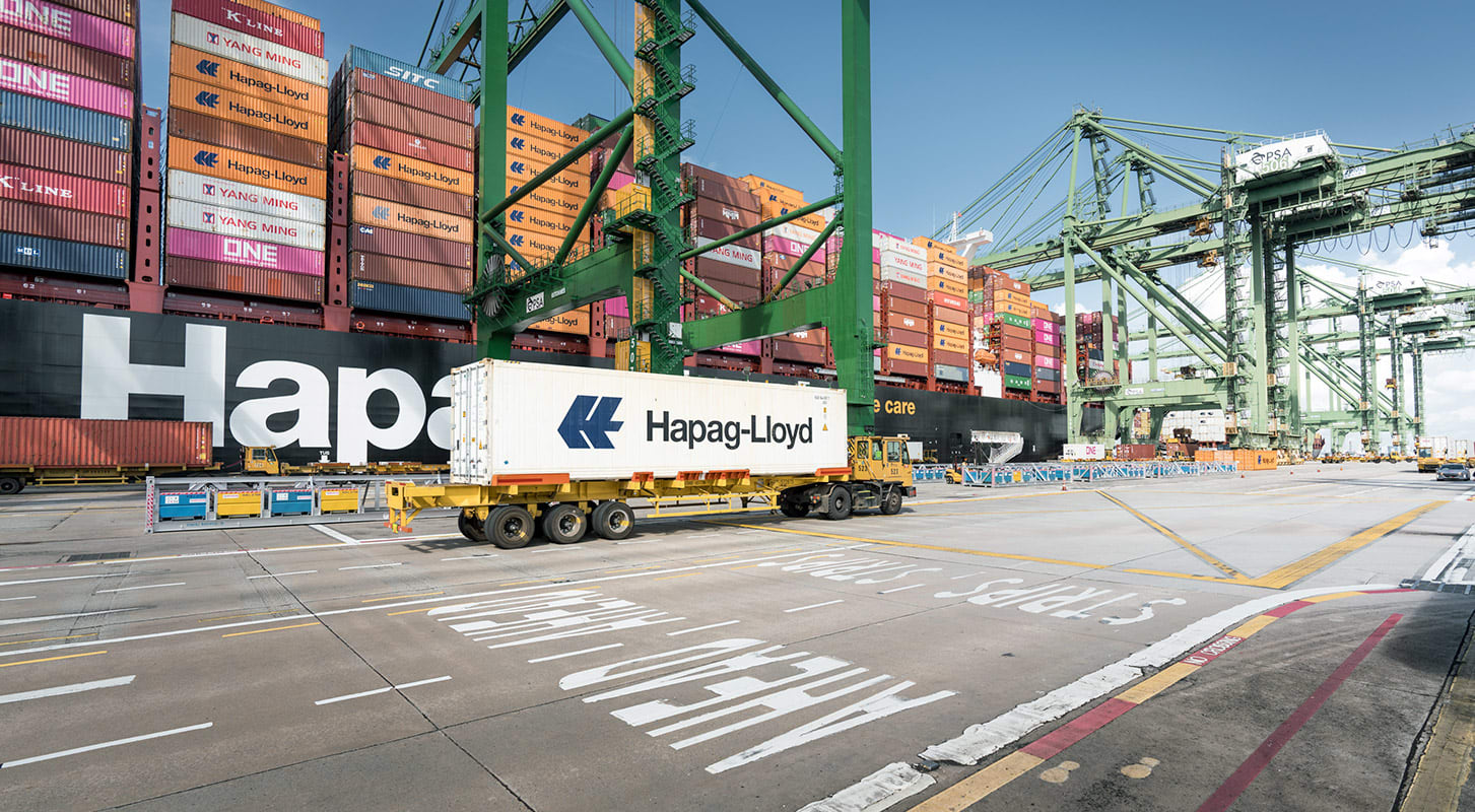 A Hapag-Lloyd truck stands parked before a container ship, highlighting the connection between land and sea transport.